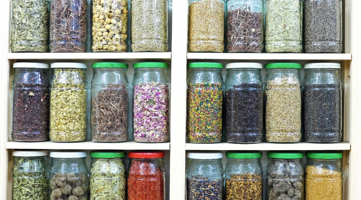 An array of transparent glass jars lines well-organized shelves, each containing a unique assortment of dried herbs. The herbs exhibit a diverse spectrum of colors and forms, showcasing the distinct characteristics of each botanical specimen, offering both visual appeal and culinary versatility.