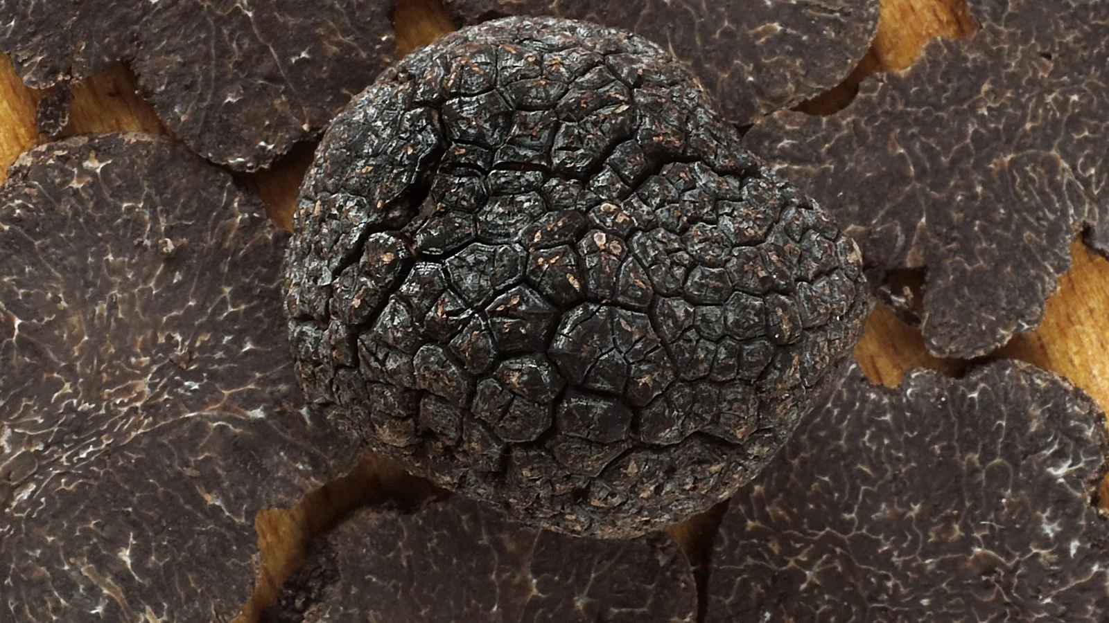 Цілий та нарізаний чорний трюфель Tuber melanosporum на дерев'яній поверхні. Вирощування трюфелів чорних сортів є можливим.