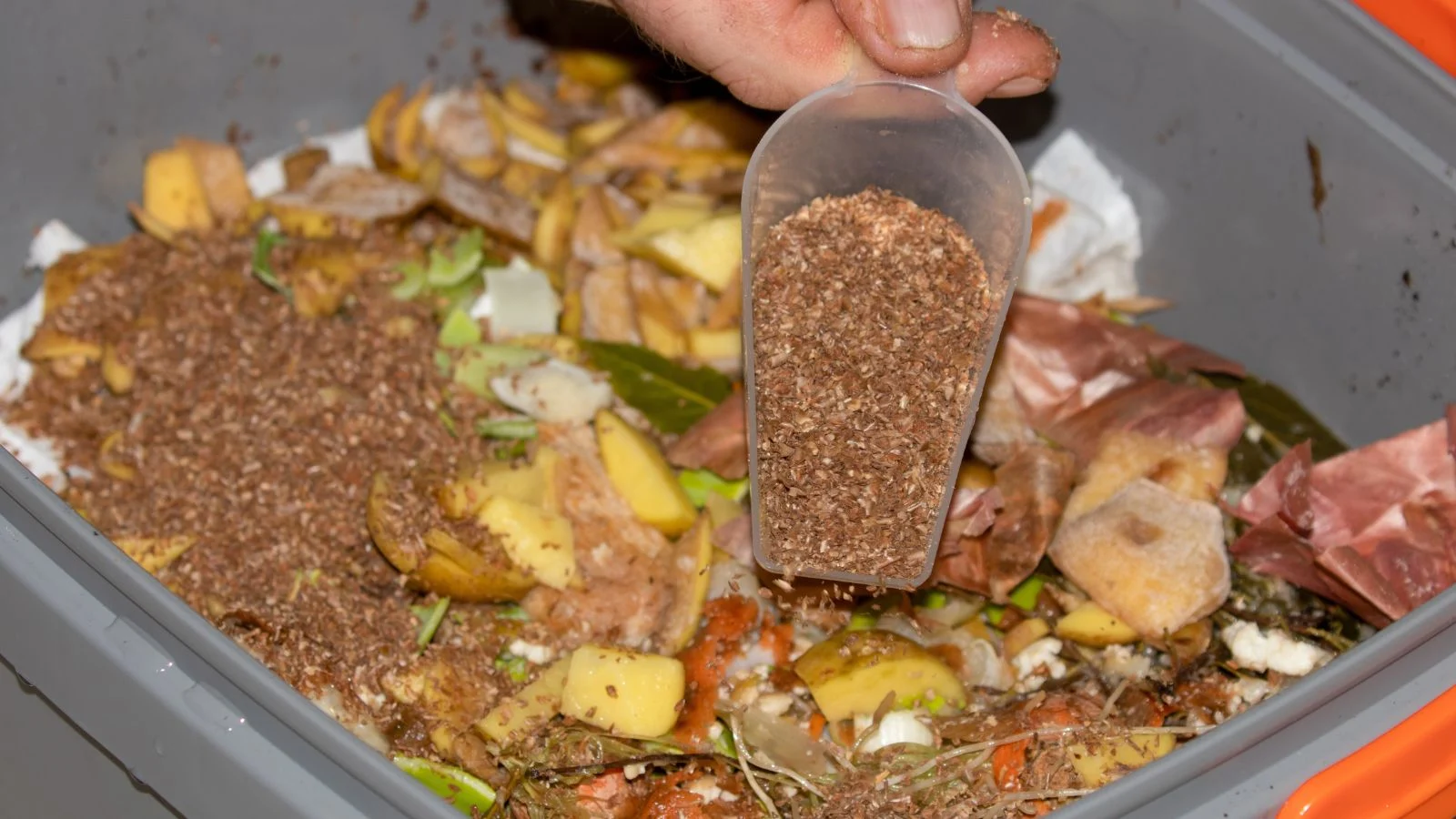 Рука тримає совок з бокаші-висівками для компостування.